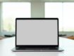 A laptop on a table in a bright, modern office space, with a blank screen.