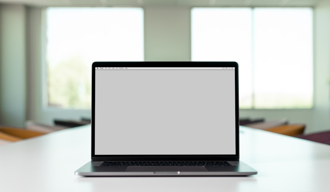 A laptop on a table in a bright, modern office space, with a blank screen.