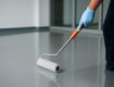 A person painting a smooth epoxy floor with a roller in a commercial space.